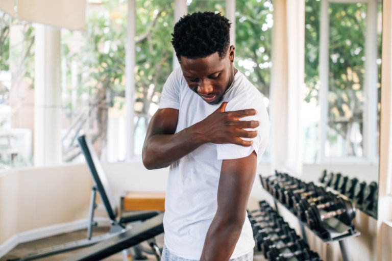 Man in a gym holding his left shoulder in discomfort