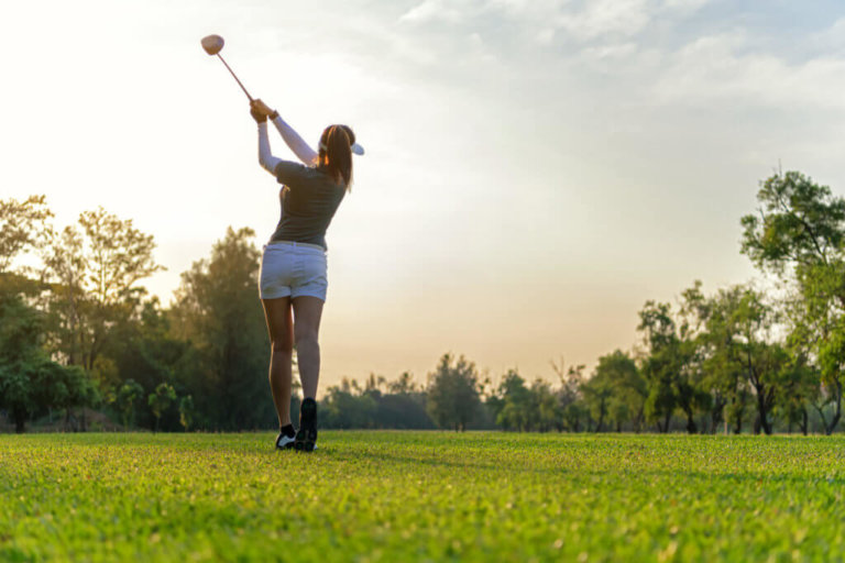 Female golfer completed golf swing on a wooded course