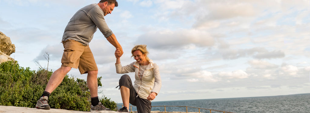 Man helping a woman onto a ledge in a nature preserve overlooking water