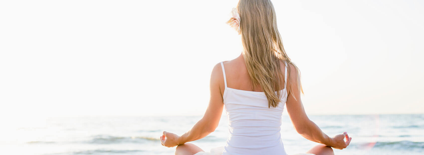 Woman in white top sitting on a beach meditating