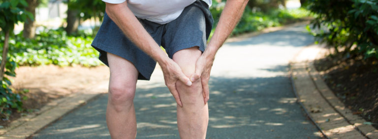 Man on outdoor path holding his left knee in pain after running