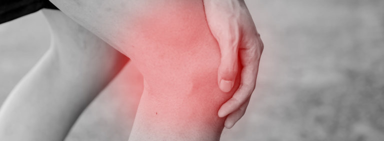 Black and white image of person holding their knee, with red glow on the knee signifying pain