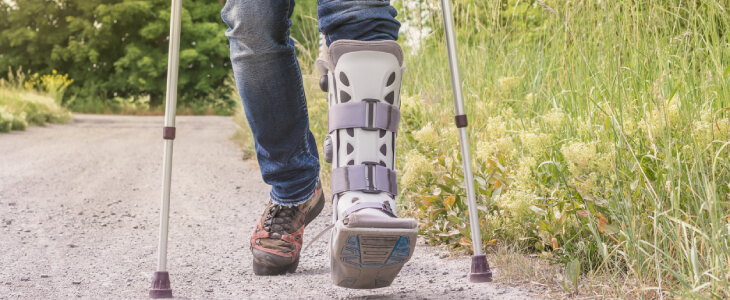 Man hiking outside with foot cast and crutches.