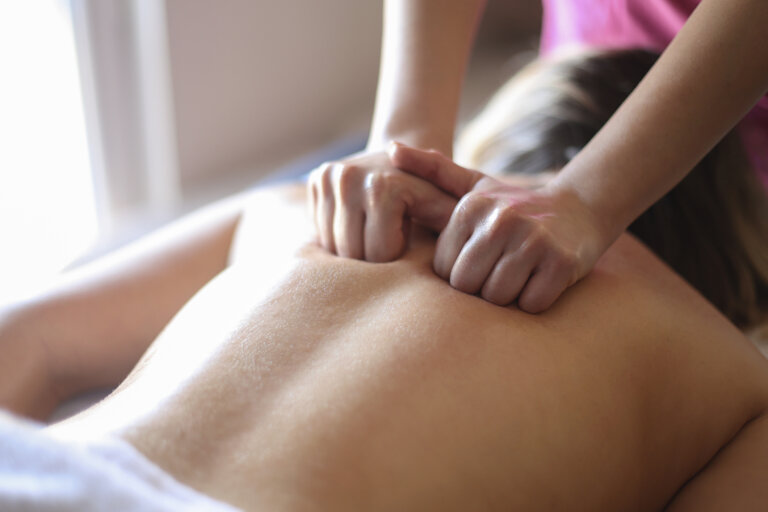 A massage therapist giving a person a back massage, focusing on the shoulders.
