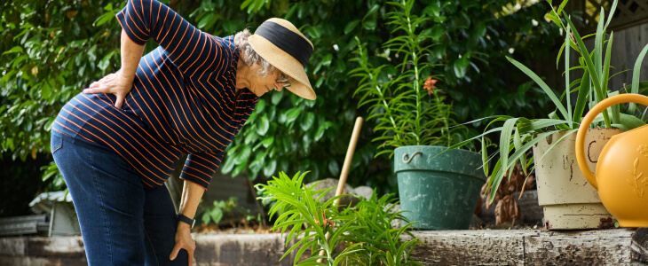 Older woman outside hunched over with hand on back in pain