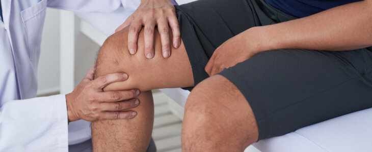 Doctor checking knee of male patient
