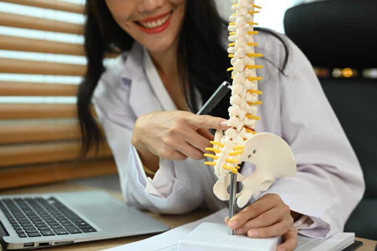 Physiotherapist showing a lumbar disc herniation with a spinal model while giving consultation at rehab clinic.