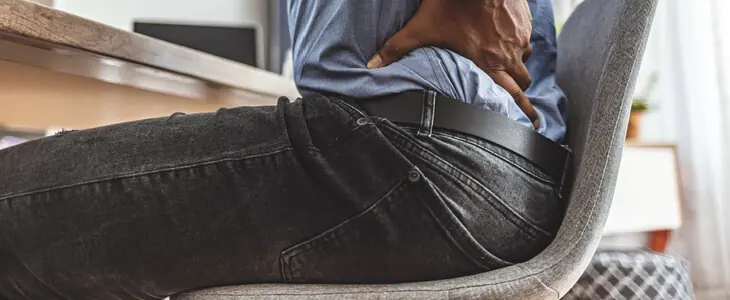 A man sitting at a desk and gripping his lower back in pain.