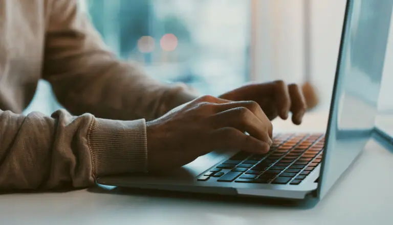 A close-up of a person's hands typing on a laptop keyboard.