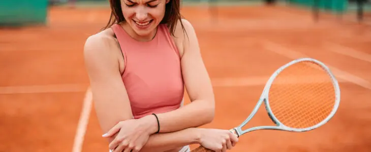 Sporty young woman holding her elbow in pain while playing tennis on a tennis court.